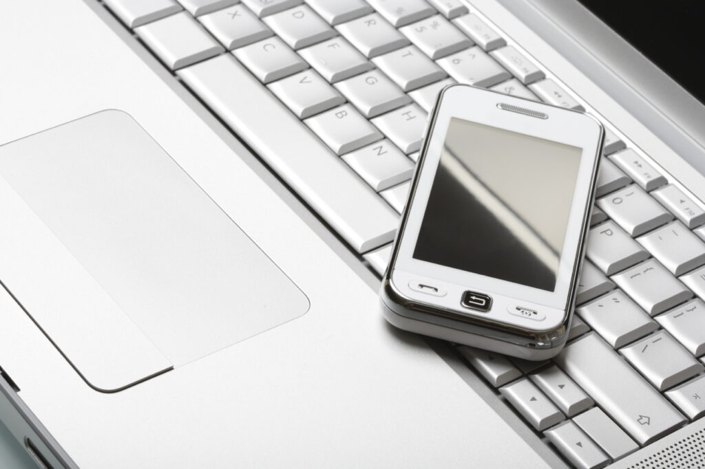 Modern communications concept. White "touch" phone (communicator) on a high-end aluminium laptop. Shallow DOF.