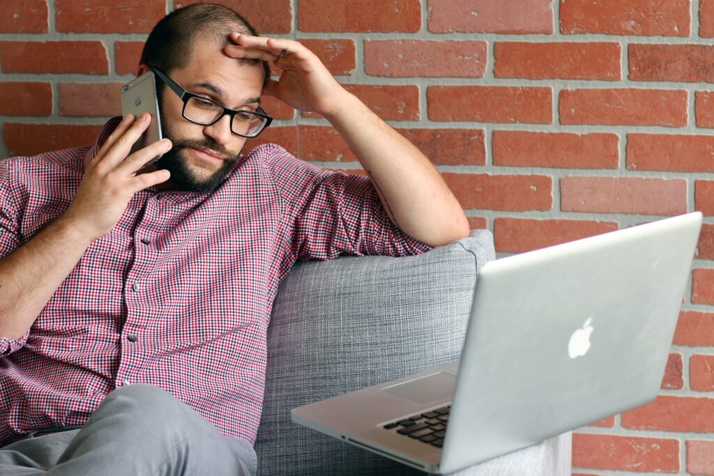 Frustrated man on phone making call to help with a laptop issue.
